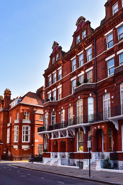 Exterior view of a multi-storey red brick residential building on Upper Street in Islington, N1, showing large windows with white frames and decorative architectural details. The ground floor features black metal balconies with ornate railings and white supporting brackets, alongside white steps leading to entrance doors. The sidewalk in front is clean, with a black bollard and street signage visible. The building's facade exhibits a classic Victorian style with brickwork and chimney stacks, illuminated by natural daylight and clear blue sky. This street scene highlights the historic architecture typical of the area, with no cleaning tools or surfaces visible, focusing solely on the building's exterior and urban setting.